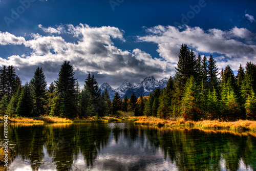 Fototapeta Naklejka Na Ścianę i Meble -  Mountain range reflecting in a tranquil lake surrounded by lush evergreen trees under a dramatic sky