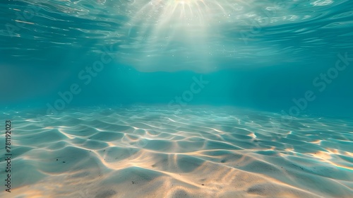 Blue tropical ocean above, seabed sand below, empty underwater background with the summer sun shining brightly, creating ripples in the calm sea water.