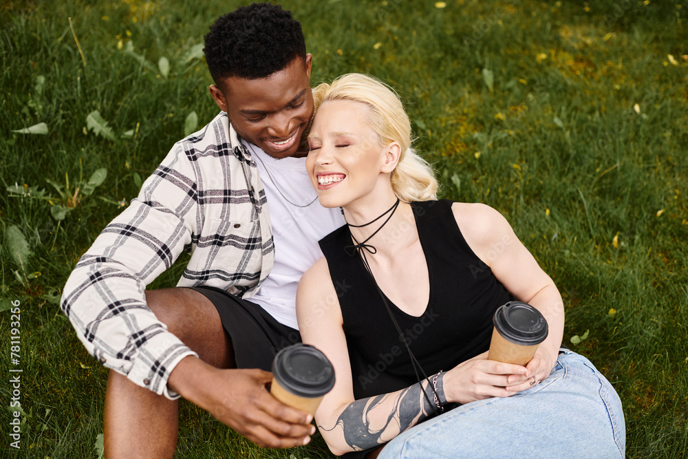 A happy, multicultural couple - an African American man and a Caucasian woman - sitting together on the grass in a park. A happy, multicultural couple - an African American man and a Caucasian woman - sitting together on the grass in a park.