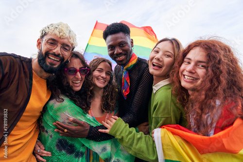Happy portrait of a multiracial group of young people celebrating Gay Pride Festival Day with rainbow flags. LGBT community concept. Men and women hugging looking at camera outdoors. photo