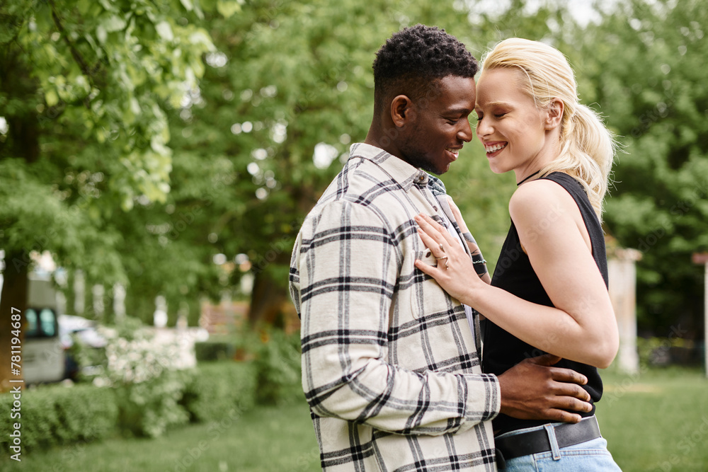 A happy African American man and Caucasian woman standing closely together in a vibrant park, showcasing love and unity. A happy African American man and Caucasian woman standing closely together in a vibrant park, showcasing love and unity.