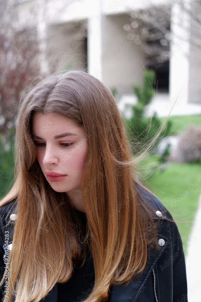 young blonde woman with long hair looks straight at the camera and to the side. beautiful woman sitting on the street. street photo shoot women young blonde woman with long hair looks straight at the camera and to the side. beautiful woman sitting on the street. street photo shoot women