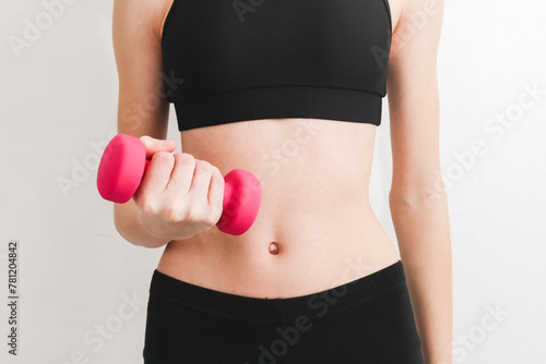 Young beautiful caucasian teen girl in a fitness suit holds pink dumbbell with one hand .