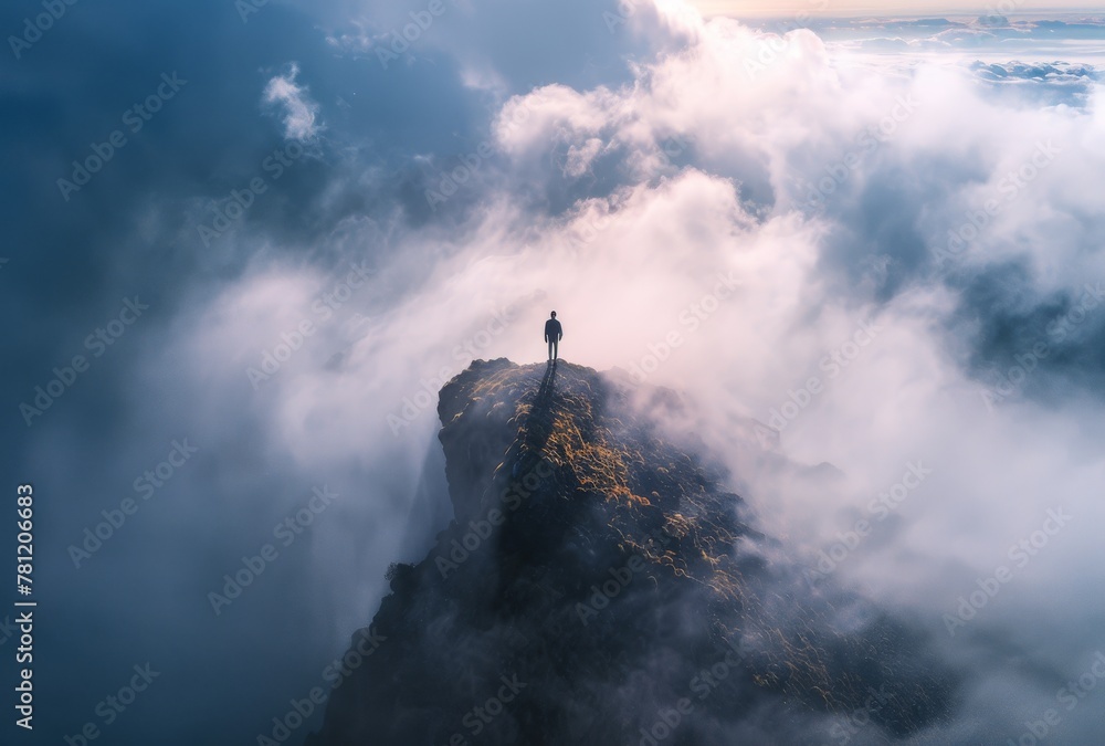 A man stands on a mountain top in the fog. The scene is serene and peaceful, with the man alone on the mountain, surrounded by the mist. The fog adds a sense of mystery and solitude to the image