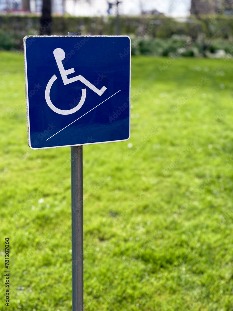 A small blue wheelchair handicap sign stands against a blurred garden background, symbolizing accessibility and inclusivity in outdoor spaces. A small blue wheelchair handicap sign stands against a blurred garden background, symbolizing accessibility and inclusivity in outdoor spaces.