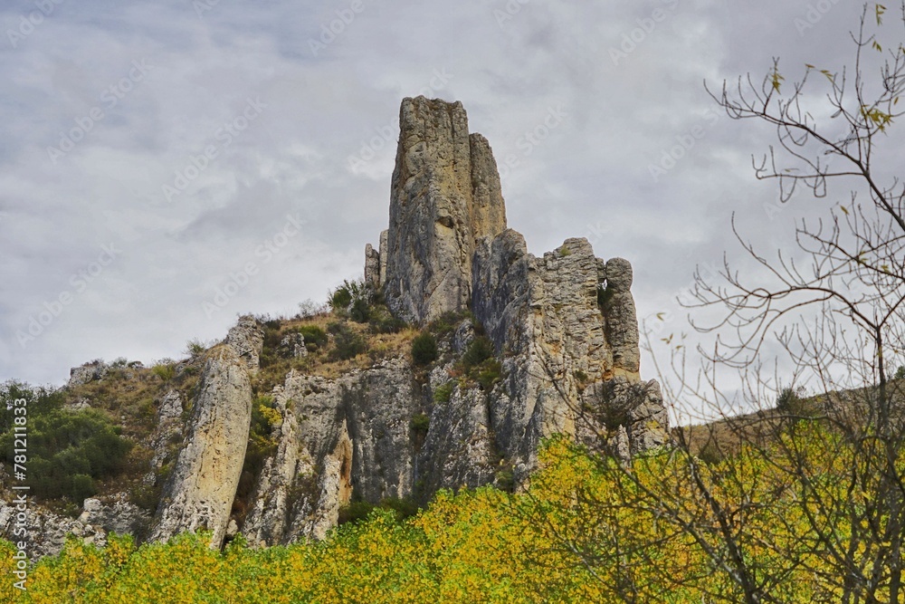 Huge rock formation surrounded by green and yellow autumn trees under cloudy sky