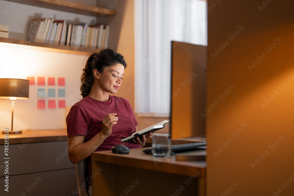 A diligent mid adult woman reading through her notes from her notebook and working from home