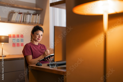 A satisfied mid adult woman watching an online seminar on her computer while writing down notes