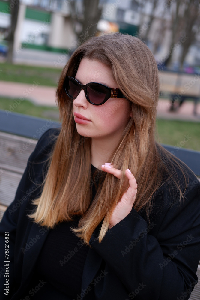 young blonde woman in a black classic jacket and black stylish sunglasses on the street. close-up portrait of a blonde woman. casual style