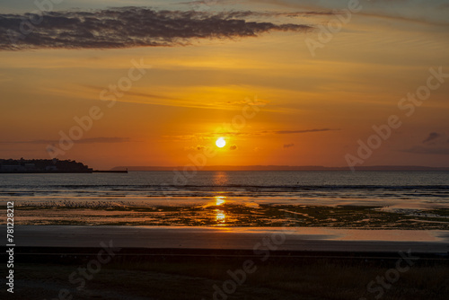 Des teintes orangées illuminent le littoral breton, où le coucher de soleil peint le sable de reflets dorés, offrant un spectacle envoûtant