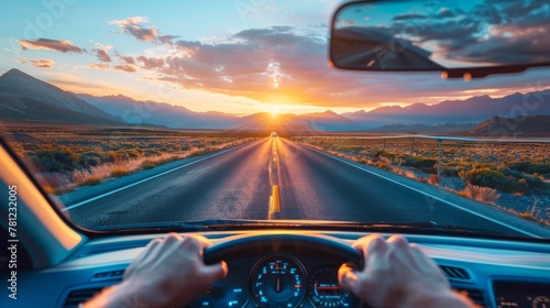 Driver's perspective on an open road journey towards a stunning sunset with mountain views.
