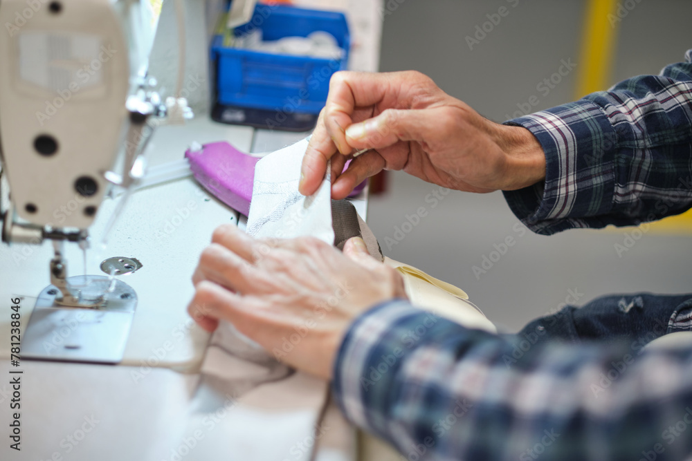 Obraz premium Hands on a sewing machine working in a textile factory industrial setting. Metal cotton sewing machine industry. Cotton sewing and fabrication textile industries. Metal hanger rails.