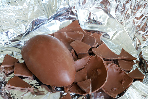 Un uovo di Pasqua di cioccolato al latte rotto in pezzi su fondo argentato. Pasqua e periodo festivo.