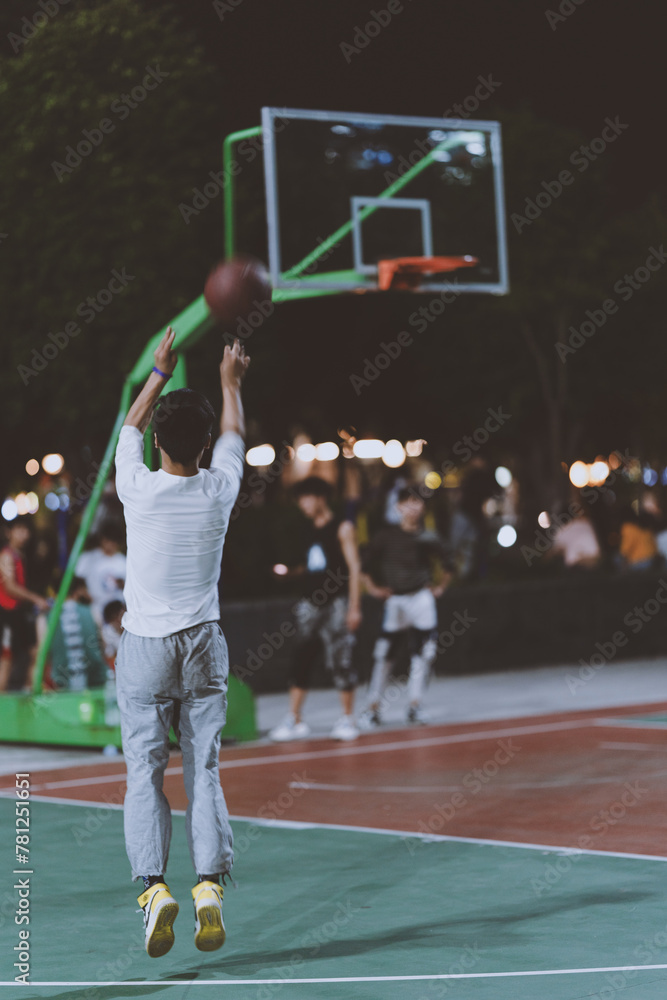 Young people are playing basketball on a basketball court in a Chinese city park. They are making shooting movements and have a standard take-off.
