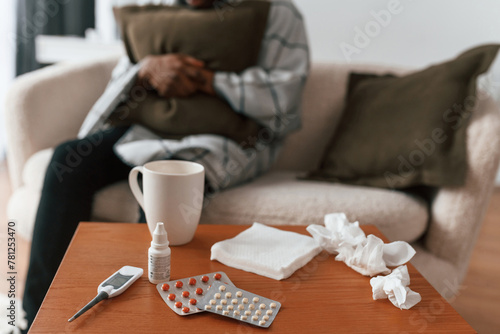 Close up view of bunch of pills on table. Sick black man is at home