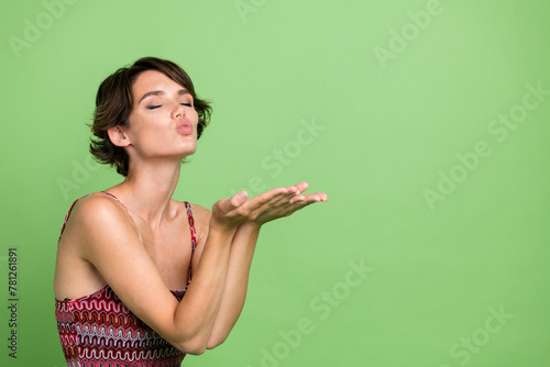 Photo of sweet adorable girl wear trendy spring clothes closed eyes kiss hold empty space isolated on green color background