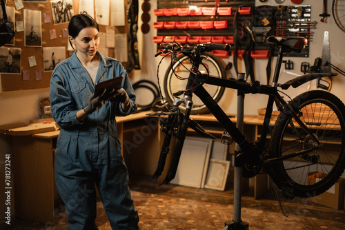 Female mechanic in a repair bike in bicycle store holding digital tablet
