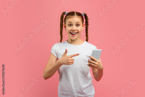Excited girl pointing at smartphone on pink background