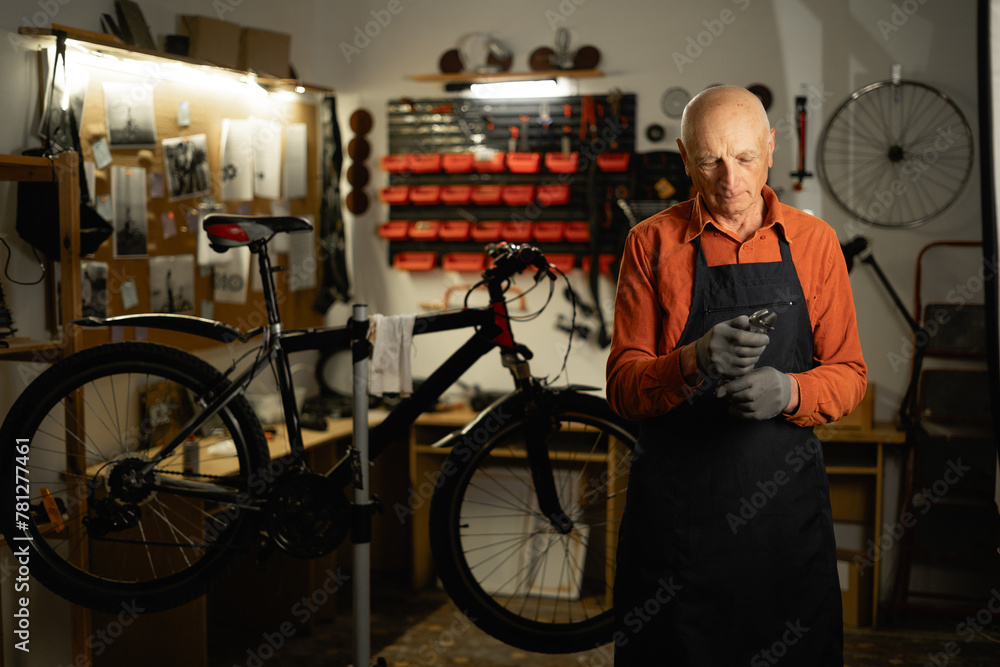 Concept of bicycle maintenance. Portrait of elderly cycling repairman holding wrench standing near bicycle in repair authentic workshop