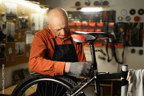 Elderly repair man in bicycle cycling workshop. Confident old bike mechanic, small business owner and mature technician. Repair and upgrade bicycle