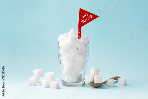 Glass full of sugar cubes with no sugar red sign on blue background, unhealthy and diabetes concept