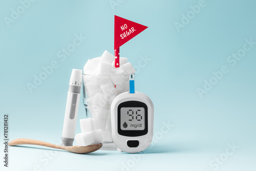 Diabetes concept, glass full of sugar cubes with no sugar red sign and blood glucose meter and lancet on blue background