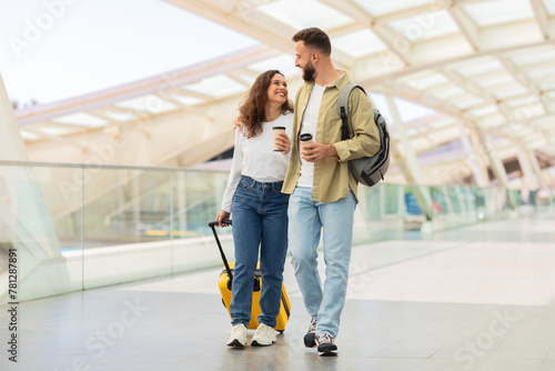 Man and Woman Walking Through Airport With Luggage And Takeaway Coffee