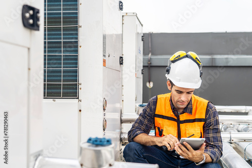 Male technical foreman in safety uniform inspects maintenance work holding a tablet to look at plumbing and electrical systems on the roof of a building, Technician man worker checking power system