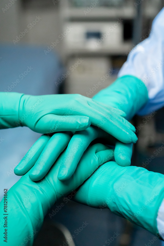 close-up of clasped hands of doctors wearing green gloves together before surgery