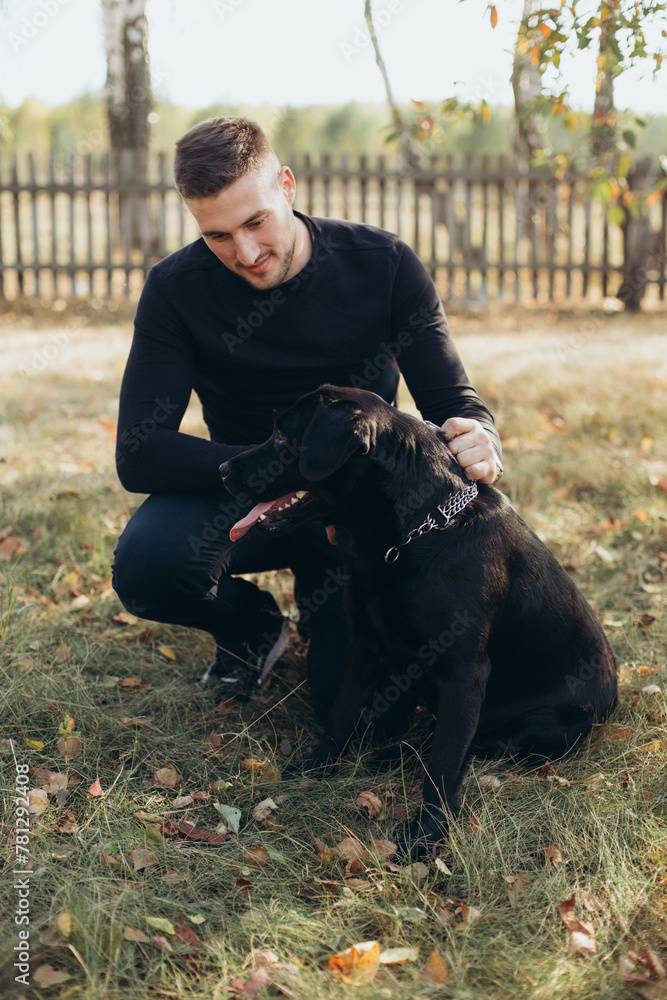 a handsome man in black clothes with a black labrador dog a handsome man in black clothes with a black labrador dog