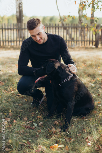 a handsome man in black clothes with a black labrador dog