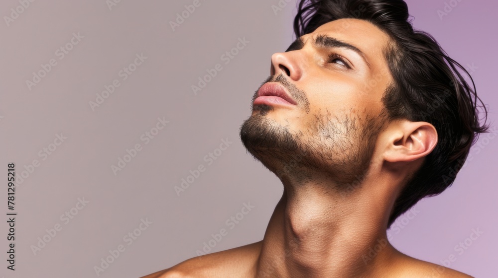 Obraz premium Handsome Young Man with Stubble Gazing Up Thoughtfully on Purple Background.