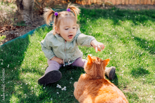 Child girl playing with ginger cat in spring garden © artifirsov