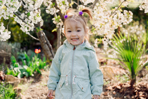 Smiling cute child girl in jacket in blooming garden. © artifirsov