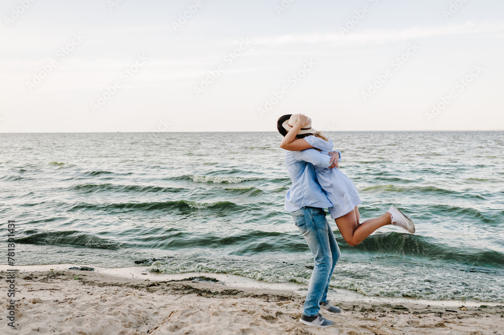 Happy and funny couple in love hugging on seashore. Female and male standing on beach ocean and enjoying sunny summer day. Man and woman embrace on sand sea. Cheerful couple spending time together. Happy and funny couple in love hugging on seashore. Female and male standing on beach ocean and enjoying sunny summer day. Man and woman embrace on sand sea. Cheerful couple spending time together.