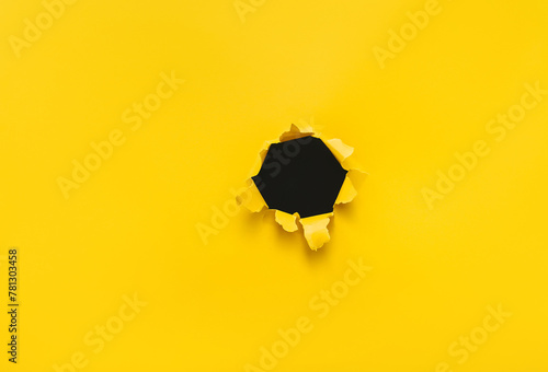 Torn hole in yellow paper with black empty background. Copy space, mockup. Place for text or logo.