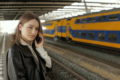 Portrait of a young woman talking on mobile phone waiting for a train at a station 