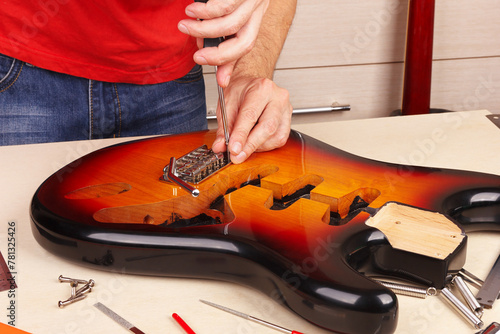 Guitar technician screws tremolo into the body of guitar.