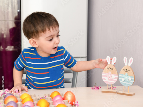 Easter, Happy Boy admiringly examines and touches the bunny's ears. There are colored eggs on the table. photo