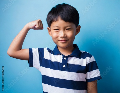 Portrait of asian little boy flexing biceps on blue background