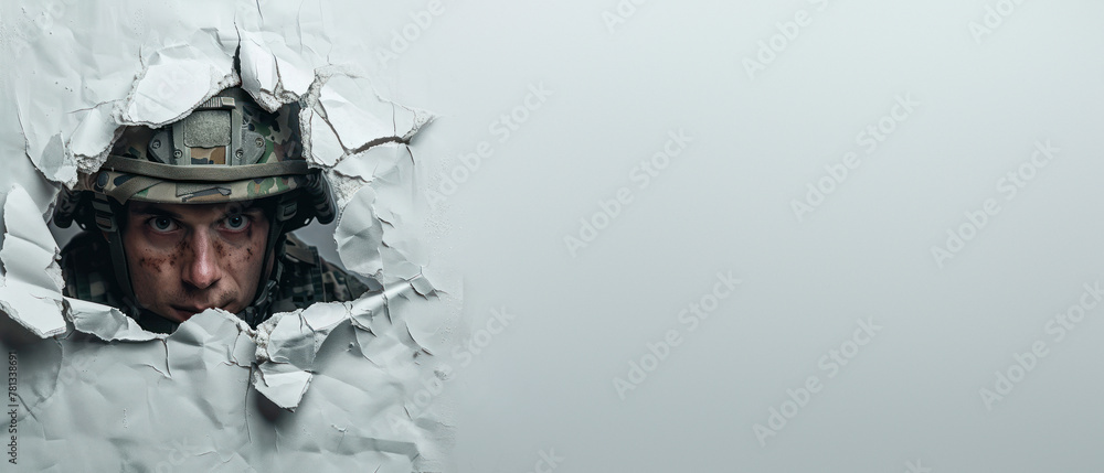 Focused soldier with a helmet peering through a white wall tear