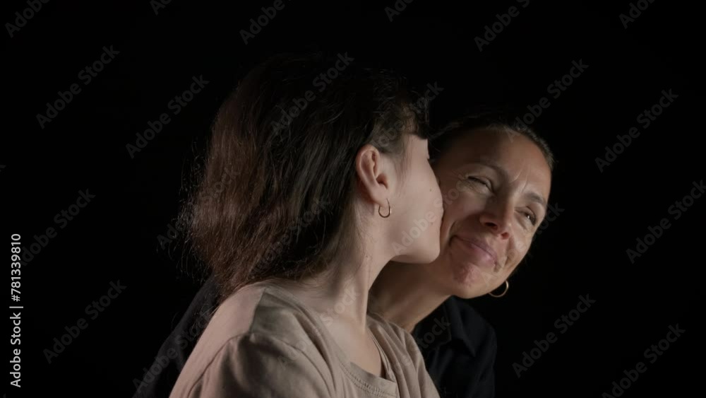 Emotional child and mom against black background. An emotional young daughter sitting by her good looking mother against black background. Emotional child and mom against black background. An emotional young daughter sitting by her good looking mother against black background.