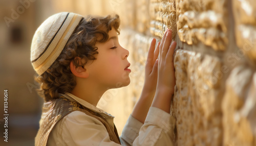 A Jewish boy in prayer: A young boy with a yarmulke kippah leans against the Western Wall in Jerusalem, deep in prayer, embodying devotion and faith. Concept of spiritual devotion and religious faith. photo