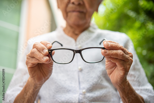 Senior Asian woman holding  eyeglasses,  eye sight problem, optometry optics ophthalmology, bad vision concept, eyeglasses close up view,selective focus.