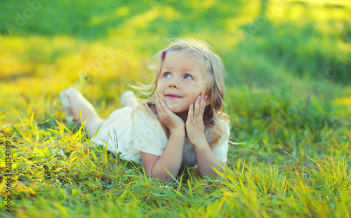 Happy little girl child lying on green grass looking up in sunny summer park