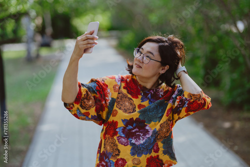 Joyful female capturing a selfie on a sunny day in the park. Happy woman taking a selfie with her mobile phone in a green city park
