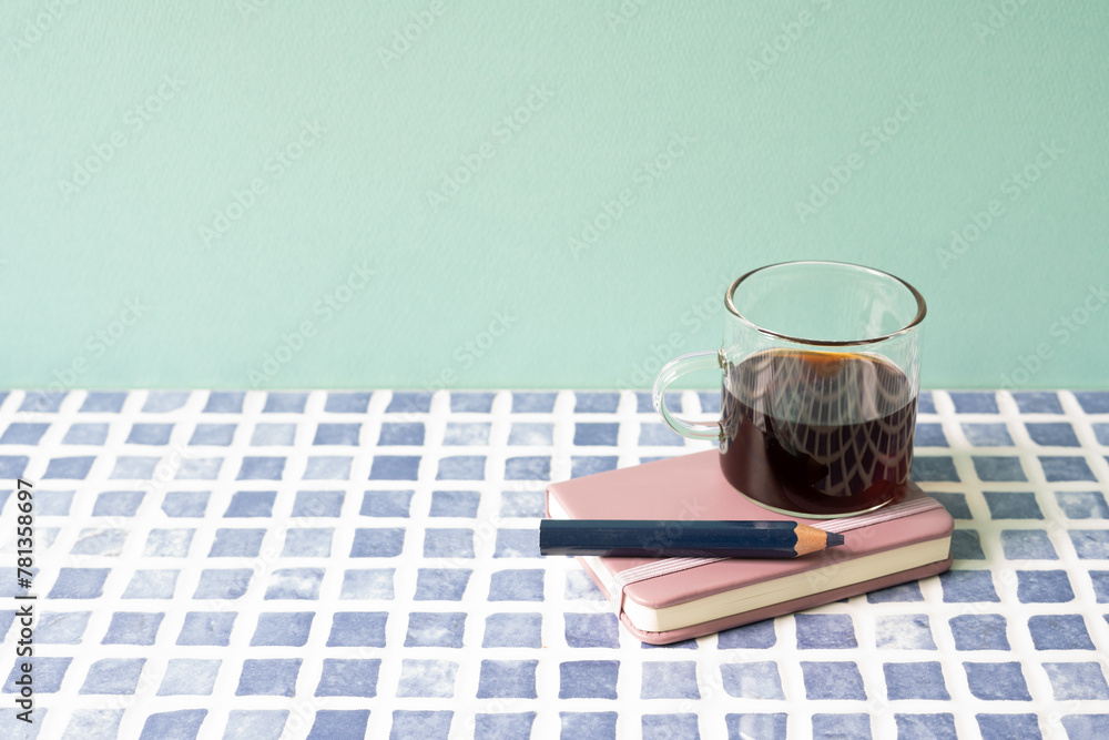 Diary notebook, pencil, coffee on blue tile desk. mint wall background. workspace