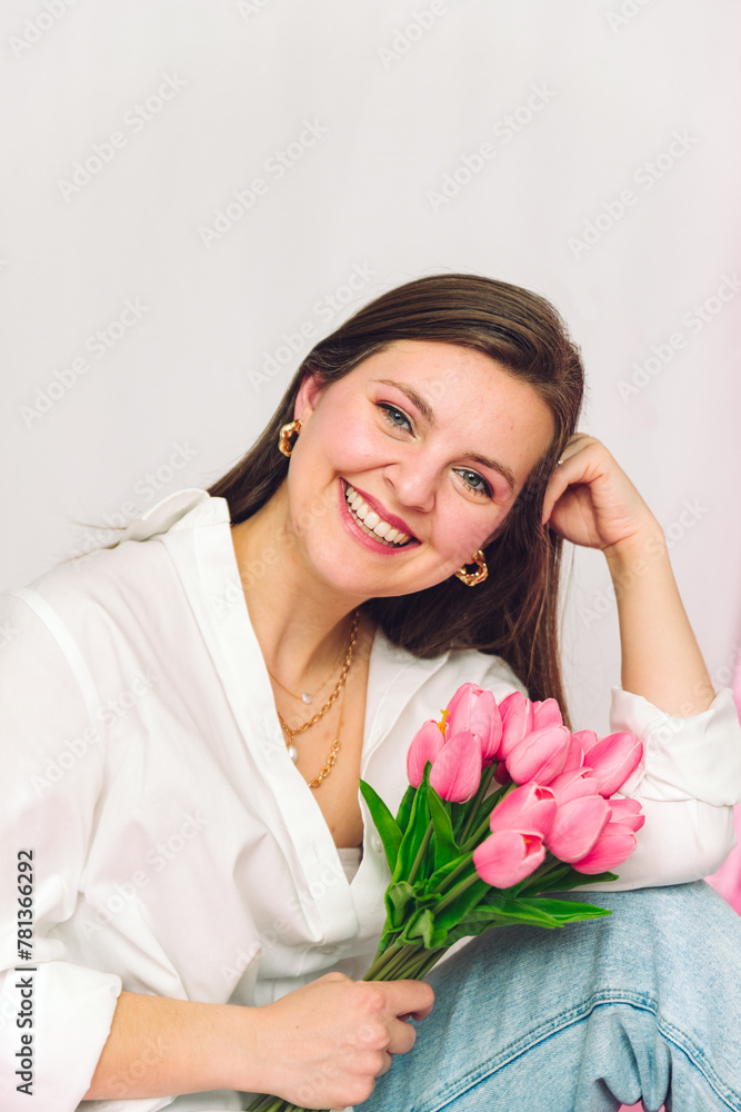 Close headshot of smiling woman holding pink flowers. Wearing gold jewelry, causal attire, jeans, white shirt, model, photoshoot, springtime. Close headshot of smiling woman holding pink flowers. Wearing gold jewelry, causal attire, jeans, white shirt, model, photoshoot, springtime.