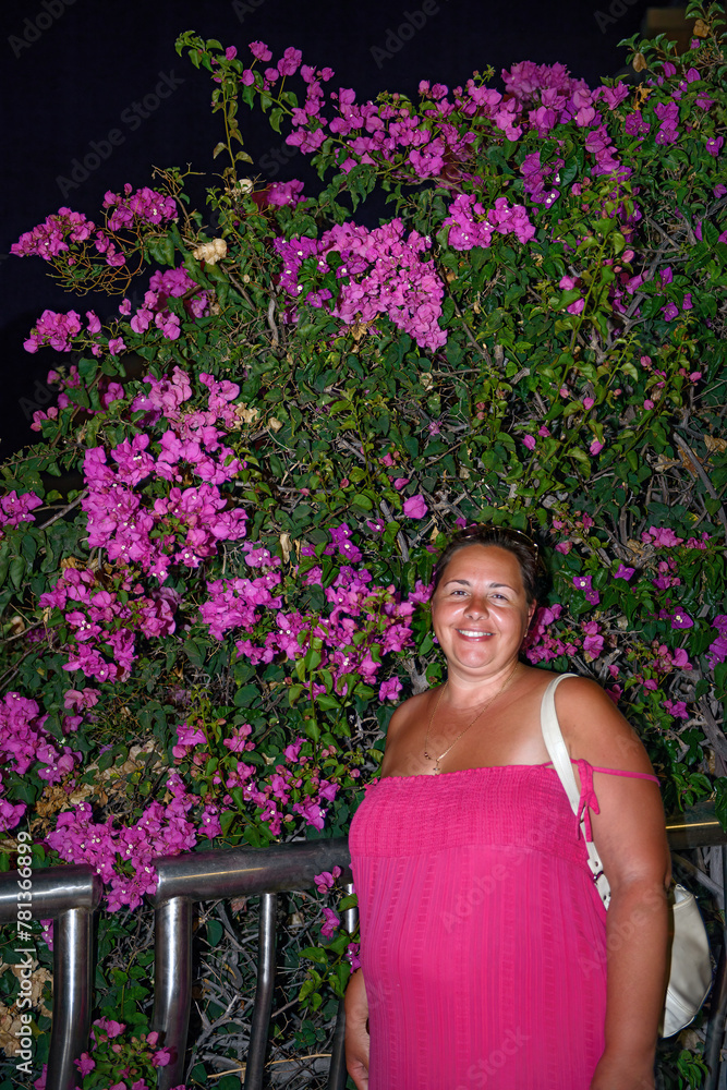 Woman is standing in night near bright bougainvillea bush. Woman is standing in night near bright bougainvillea bush.