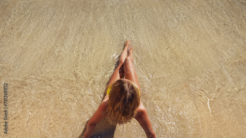 A young woman in a blue bikini sot on the sand near the waves of the blue sea. View from above. photo